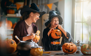 Obraz premium Happy Mother and Daughter in Witch Costumes Carving Pumpkins