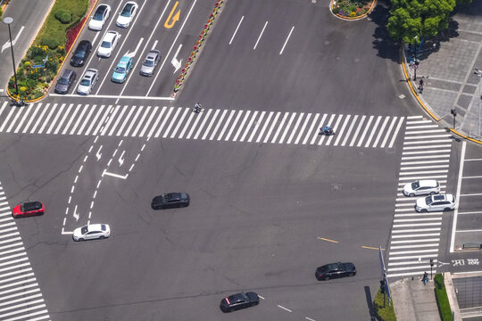 High angle view of a wide downtown crossroads with buses and cars in motion, an overhead gantry standing above the marked approach, a planner's view of junction capacity.