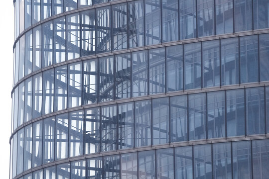 Close overhead view of sweeping glazing and interior floors of an office tower, reflections of the district sliding across the curved glass, the painted rules of a crowded district.