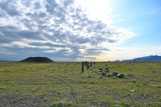 Ancient Besshatyr kurgan burial mound complex in Altyn-Emel National Park. Sacral archaeological site with stone menhirs, burial mounds and distant mountains under a blue summer sky.