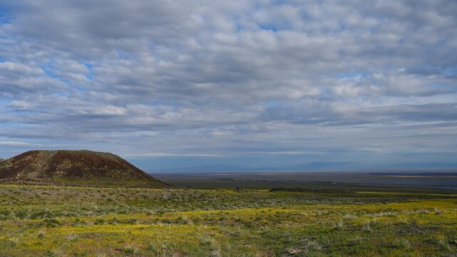 Ancient Besshatyr kurgan burial mound complex in Altyn-Emel National Park. Sacral archaeological site with stone menhirs, burial mounds and distant mountains under a blue summer sky.