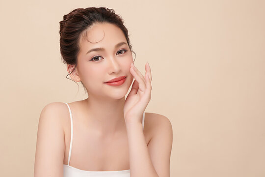 A beautiful young Asian woman with clean, fresh skin against a beige background. Skincare, facial treatment, cosmetology, beauty, and spa. An elegant portrait of an Asian woman.