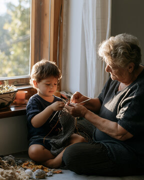 Grandmother teaching her grandchild to knit by a window