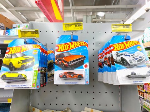 Malang, Indonesia - July 18, 2026: Multiple packaged Hot Wheels die-cast cars hanging on display hooks at a store shelf, featuring yellow, orange, and white models.