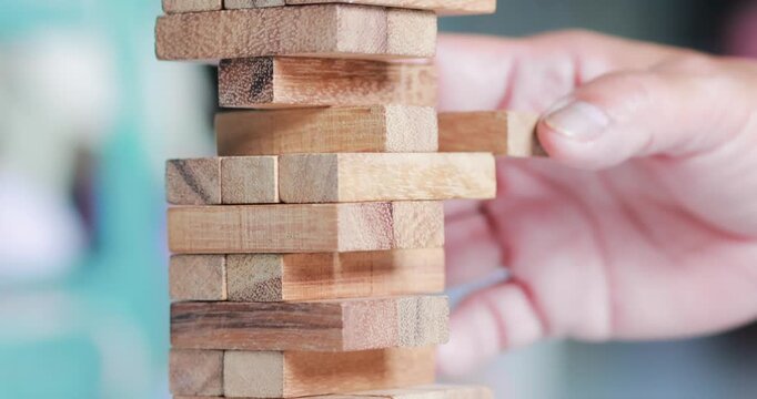Hand removing a wooden block from a stacking tower game, strategy, decision making, risk, balance, problem solving, teamwork, and business concepts, close-up
