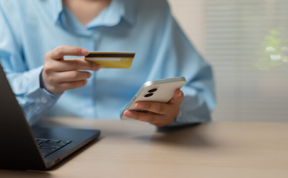 Online shopper using smartphone and credit card beside laptop for secure digital payment, mobile banking, ecommerce checkout and cashless transaction, representing modern financial technology.