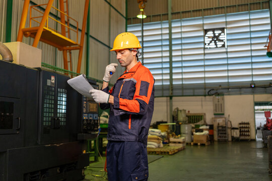 Engineer factory worker helmet uniform machine document radio industrial safety male technician reading checklist near equipment factory workshop