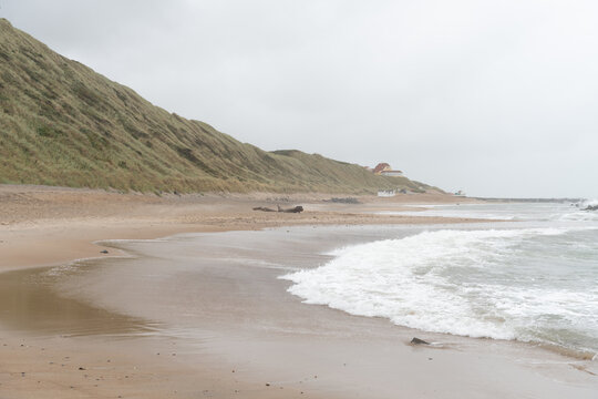 Quiet misty beach with waves and dunes in the distance