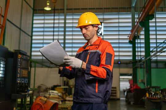 Engineer factory worker helmet document safety uniform industrial machinery workshop male engineer reading paper document with focused expression