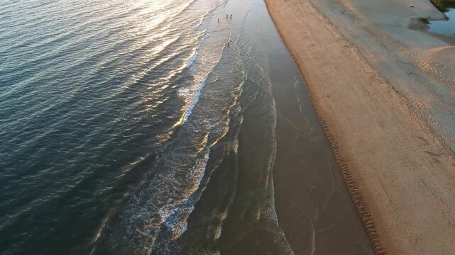 Aerial view of traditional shellfish gatherers working on a sandy beach during a beautiful low tide sunset in tavira, algarve, portugal, with ocean waves crashing on the shoreline