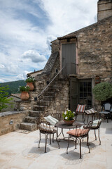 Naklejka premium Sunny Outdoor Terrace With Table And Chairs Beside A Rustic Stone Building Overlooking Countryside