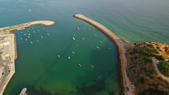 Stunning aerial perspective capturing the entrance to albufeira marina, where numerous boats are anchored in the calm, emerald waters of the algarve coastline during a beautiful sunny day