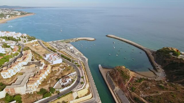 Beautiful aerial view flying towards the entrance of the albufeira marina on the stunning algarve coastline in portugal, showing the breakwaters, harbor, and surrounding cityscape on a sunny day