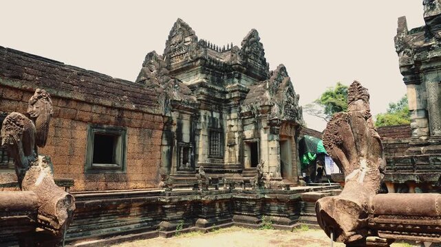 Wide low-angle view of ancient stone temple ruins with carved pillars and statues at Angkor Wat archaeological site in Cambodia during daytime.
