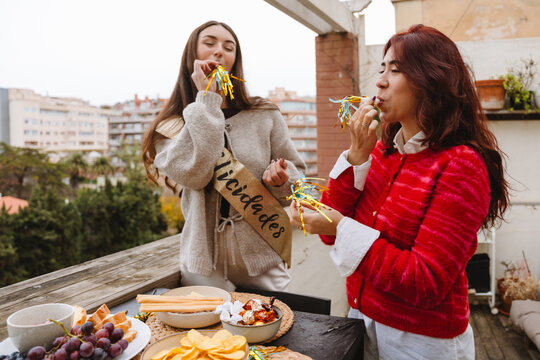 Two female friends blowing party horns at a birthday party on an apart