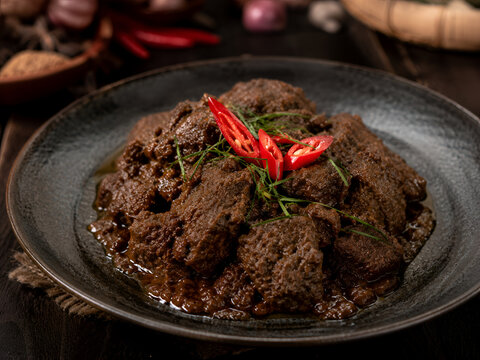 Traditional Indonesian beef rendang served on dark ceramic plate with fresh red chili garnish and rich spices
