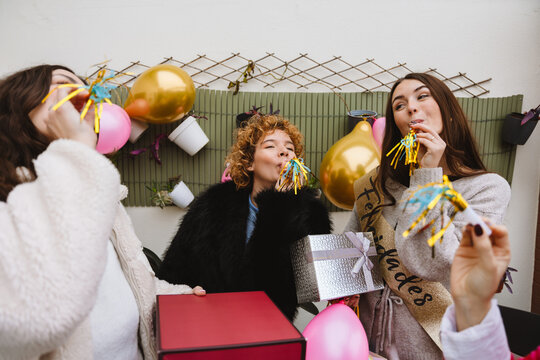 Two female friends blowing party blowers at a birthday party on an apa