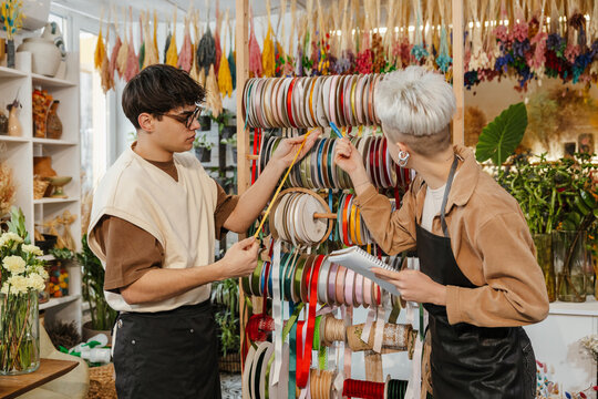 Two young florists measuring ribbon in a colorful flower shop