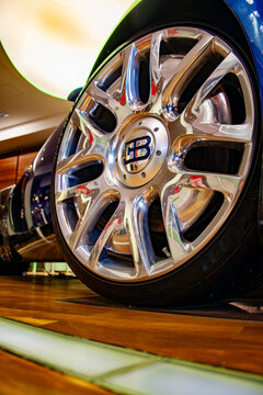 Extreme close-up of a polished chrome Bugatti wheel with the "EB" logo on the center cap, mounted on a blue Bugatti Veyron, reflections of the showroom visible in the rim.