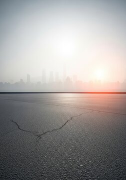 Empty Cracked Asphalt Road with Foggy City Skyline at Sunrise, Urban Environmental Concept