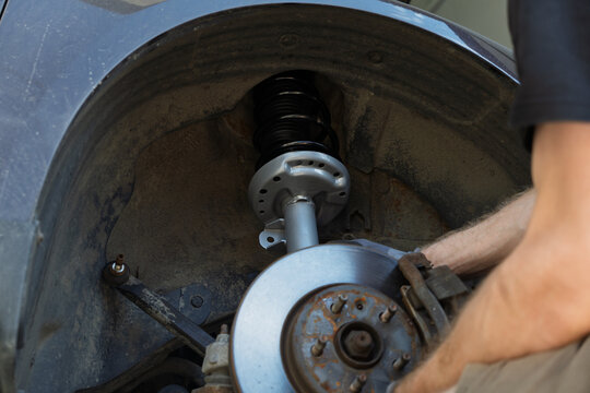 Mechanic hands inspecting a front brake disc rotor, wheel hub studs while replacing a new suspension strut shock absorber on a car wheel well during a repair process in a workshop, vehicle parts. 