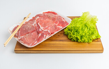 Fototapeta premium Sliced raw meat in tray with green lettuce and chopsticks on wooden board isolated on white