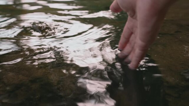 Close up of left hand touching clear stream water in morning forest, cupping and pouring water slowly, feeling nature freshness and mindfulness conceptิ