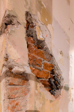 Exposed red brick wall with crumbling plaster and old pipes, raw architectural texture background with copy space.