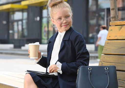 A little girl, elegantly dressed in a business suit, smiles at the camera