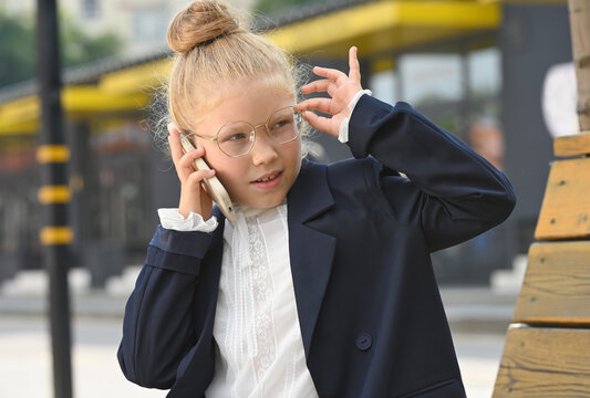 A little girl dressed in a business suit is talking animatedly on a smartphone