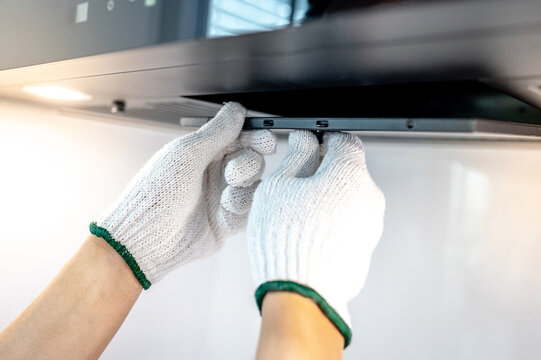 Male hand technician removing range hood filter from modern cooker hood. Maintenance worker in protective gloves installing black metal filter on kitchen hood. Home appliance repair service