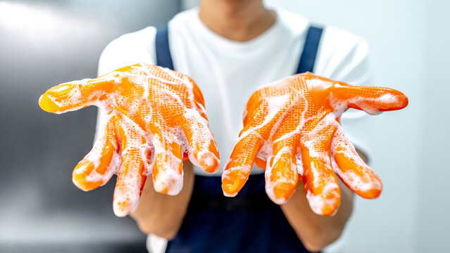Male housekeeper showing hands with orange rubber glove full with soap suds after cleaning in the kitchen. Cleaning for hygiene. Wet work household chores
