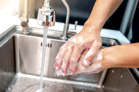 Washing hands with soap and running water from faucet on stainless steel kitchen sink. Hand hygiene after doing housework chores