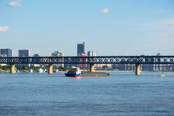 Obraz premium A cargo ship sails on the Yangtze River under the large steel bridge in the city of Wuhan China during a bright sunny day