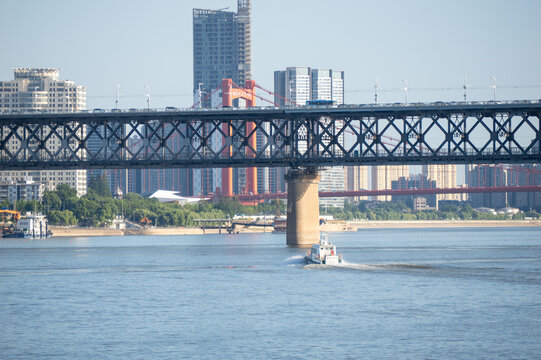 A small boat travels on the Yangtze River under the large steel bridge in the city of Wuhan China on a clear sunny day