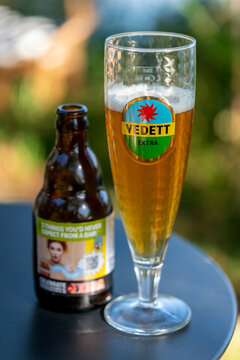Dordrecht, Netherlands - 7 September 2025: Chilled Vedett Extra beer stands beside its bottle on an outdoor table, with lush greenery creating a soft, summery backdrop, a refreshing summer drink scene