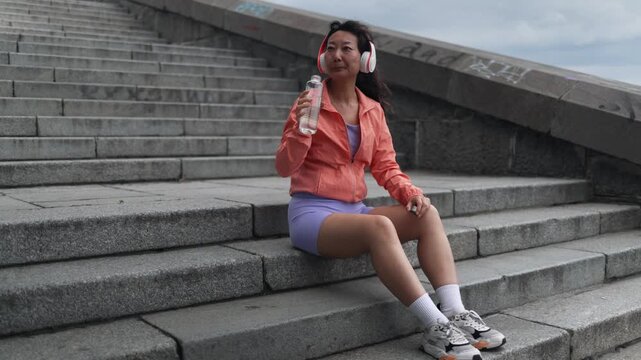 Asian woman drinking water, fitness and city for exercise, running break and health, energy or workout. Young thirsty athlete, tired runner or sports person with a bottle for outdoor training.