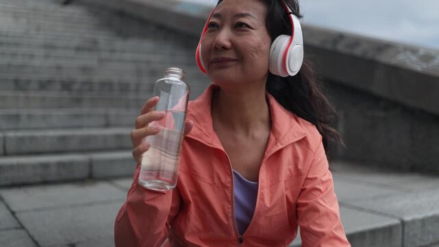 Asian woman drinking water, fitness and city for exercise, running break and health, energy or workout. Young thirsty athlete, tired runner or sports person with a bottle for outdoor training.