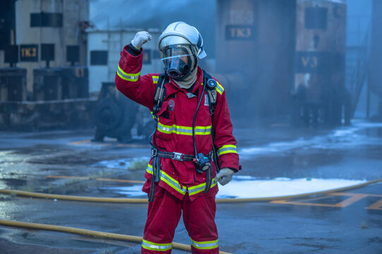 Determined male firefighter in full protective gear and helmet giving a clear hand signal to increase water pressure during an active fire suppression operation