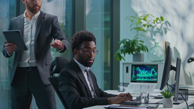 Two multiethnic business men diversity businessmen in office. African American manager intern working computer Caucasian boss leader coming checking work results satisfied support good job going away