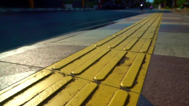 Static shot of yellow tactile paving blocks guiding a sidewalk path along a city street in the historic old town district of Gresik, Indonesia.