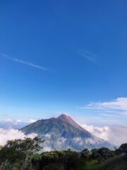 Fototapeta premium Majestic view of Mount Merapi volcano rising above sea of clouds against clear blue sky in Indonesia, great shoot, best time.