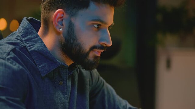 Arabian happy business man overtime night working with laptop in company office. Indian businessman male guy professional programmer work with computer cyberspace corporate software at dark evening