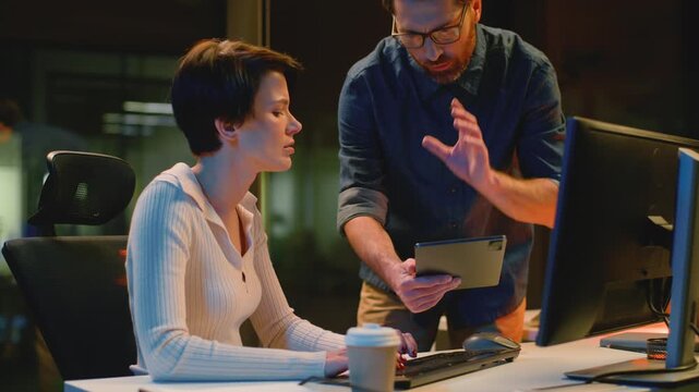 Business team quarrel talking with computer and digital tablet in dark night office. Boss man coming arguing scolding to woman intern working online late time businessman argue talk with businesswoman