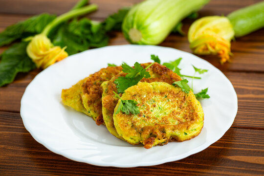 Healthy homemade zucchini fritters with edible blossoms on kitchen background