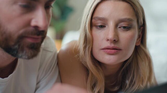 Relaxed Caucasian couple together scrolling social media digital tablet talking browsing web net in bed. European man with woman husband with wife chatting talk buying purchase online with device