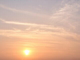 Fototapeta premium Beautiful soft pastel sky with the sun setting, casting warm orange and pink hues on wispy cirrus clouds. A peaceful natural background for various creative projects