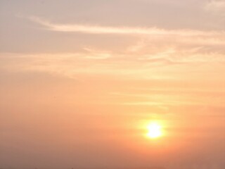 Fototapeta premium Beautiful soft pastel sky with the sun setting, casting warm orange and pink hues on wispy cirrus clouds. A peaceful natural background for various creative projects