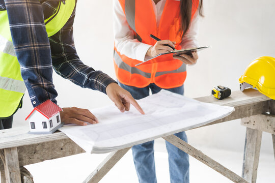Builder team, two asian young engineer woman, male architect discussing construction on blueprint, follow project to build industrial plan on bench at house site. Engineering worker, teamwork people.