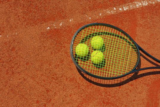 A yellow tennis ball and tennis racket lies on the clay court.